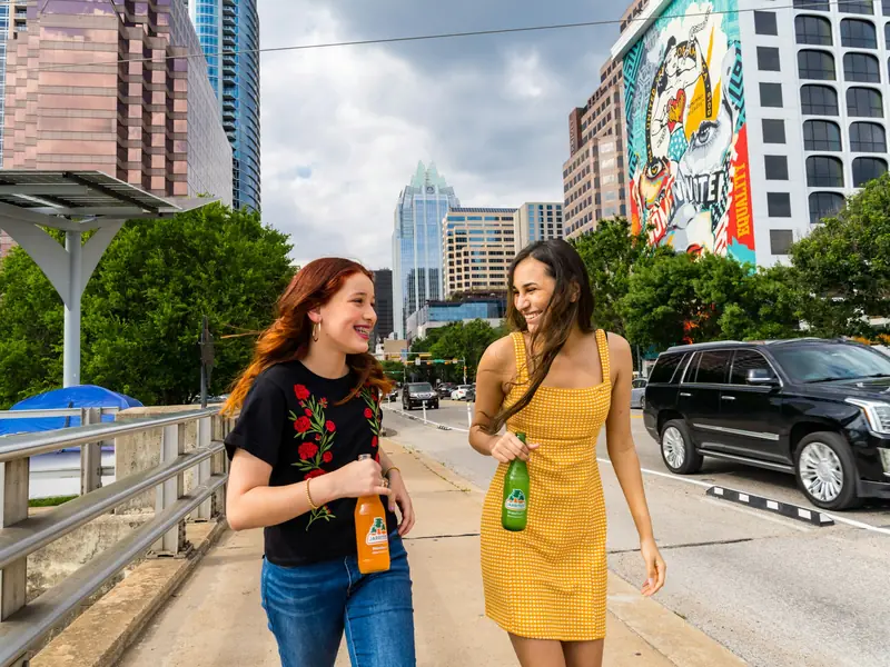 Two friends laughing as they walk across a bridge with the Austin skyline behind them