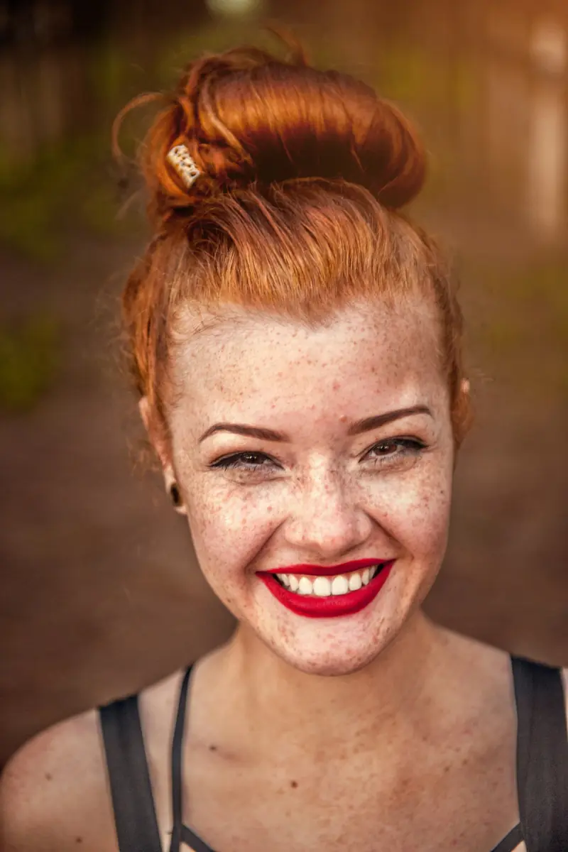 A woman with freckles and red lipstick smiling widely