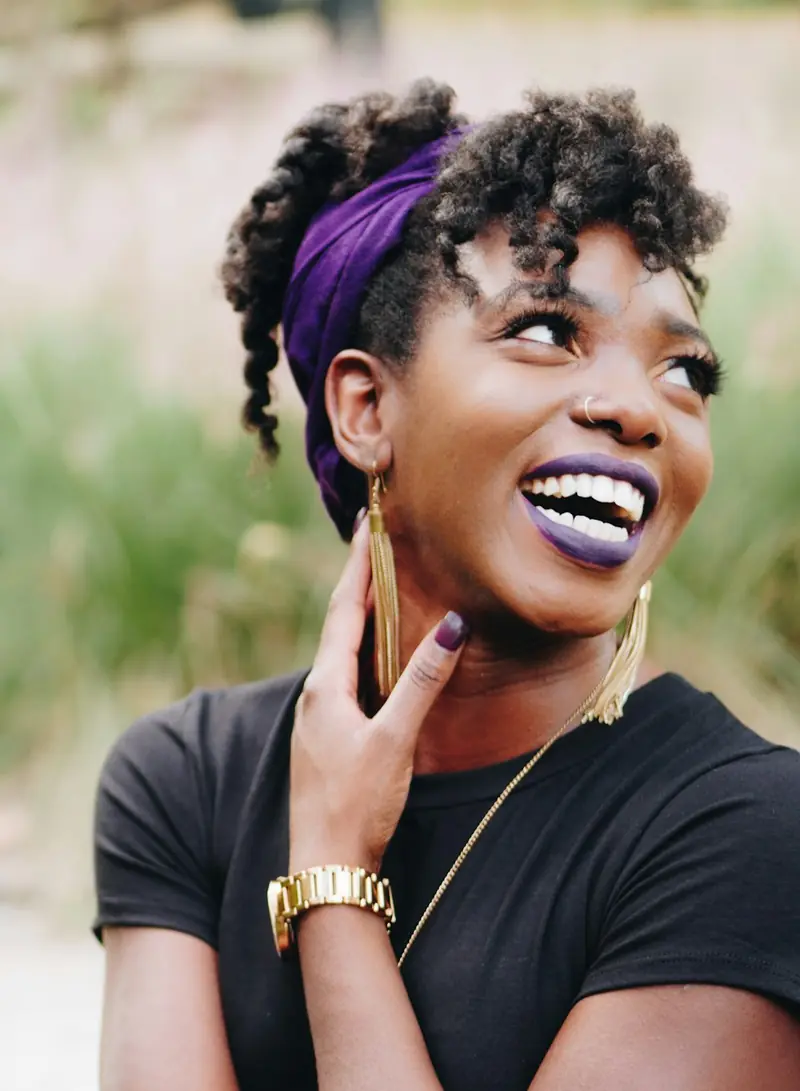 A woman in a purple headwrap laughing and looking up
